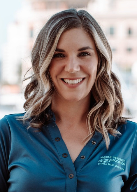 Professional headshot of a smiling woman with shoulder-length wavy hair wearing a blue Marine Industries Association of Palm Beach County polo shirt.