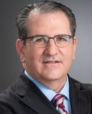 David Markarian, Chair, professional headshot wearing a suit and glasses against a gray background.