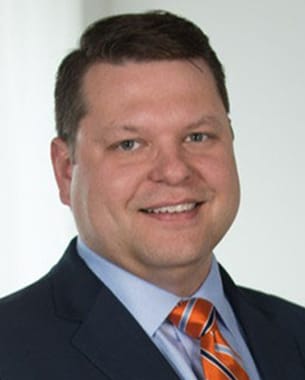 Christopher Cothran, professional headshot wearing a suit, light blue shirt, and orange striped tie.
