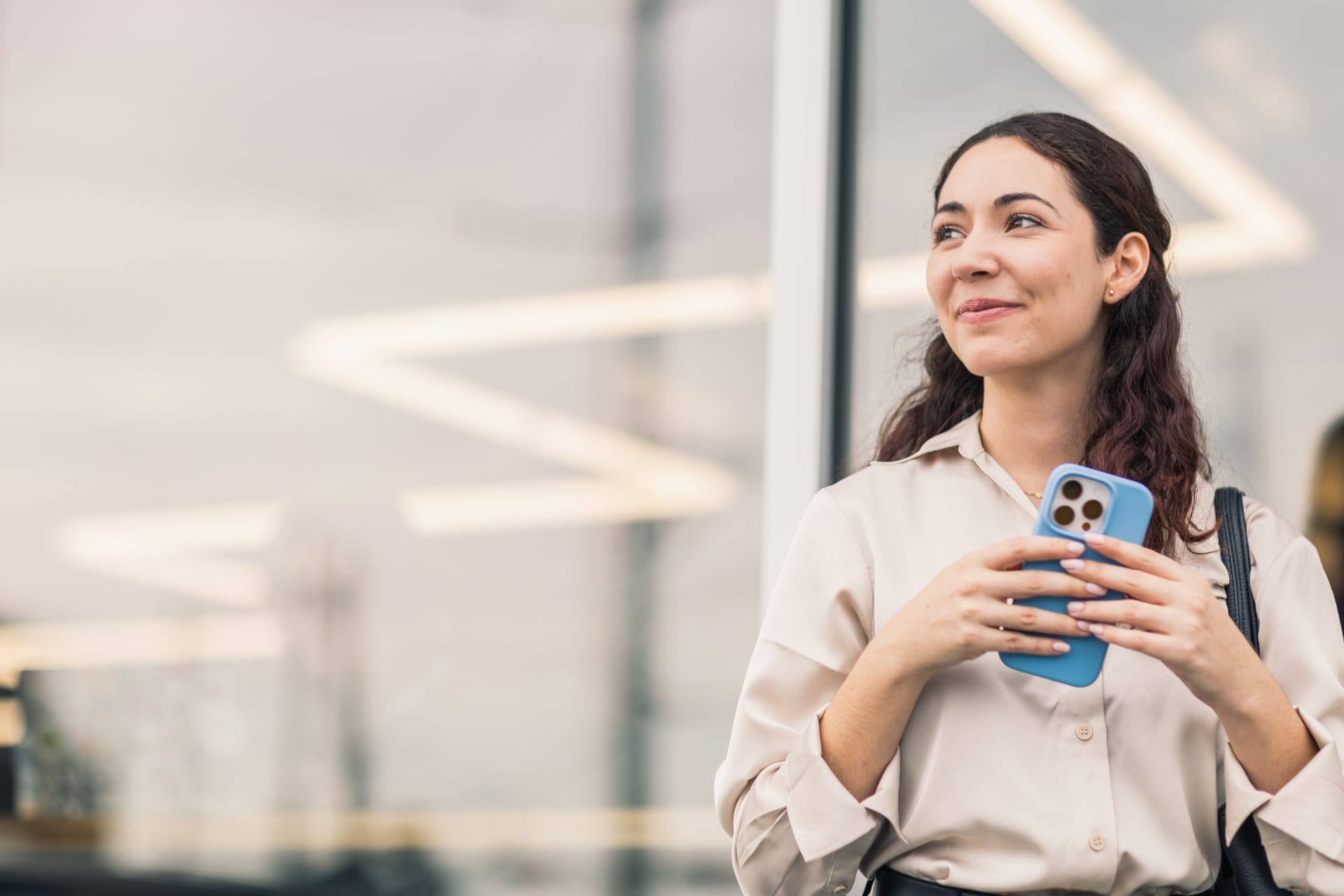 Smiling woman holding a smartphone, appearing confident and ready to take the next step in her career.