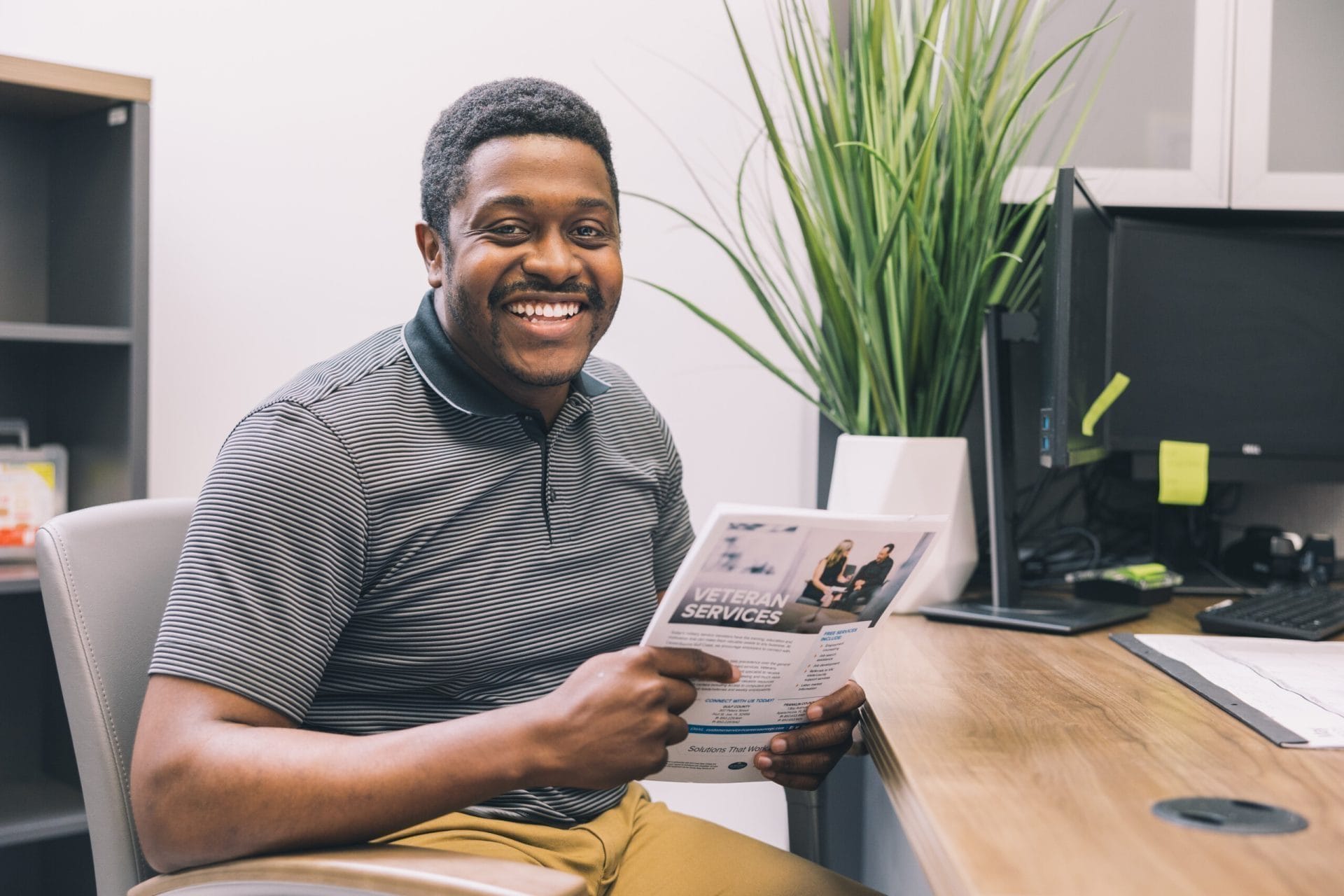 Smiling man sitting and holding a booklet, representing engagement and community connection.