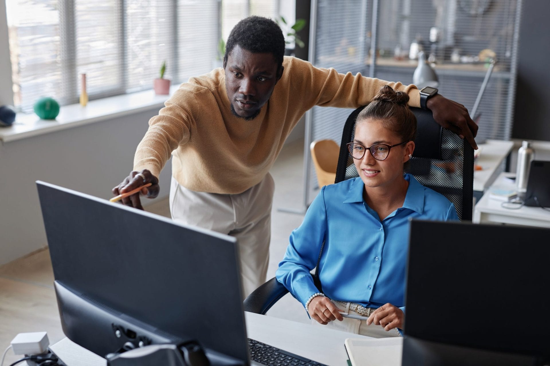 Colleague assisting another by pointing at a computer monitor in an office.