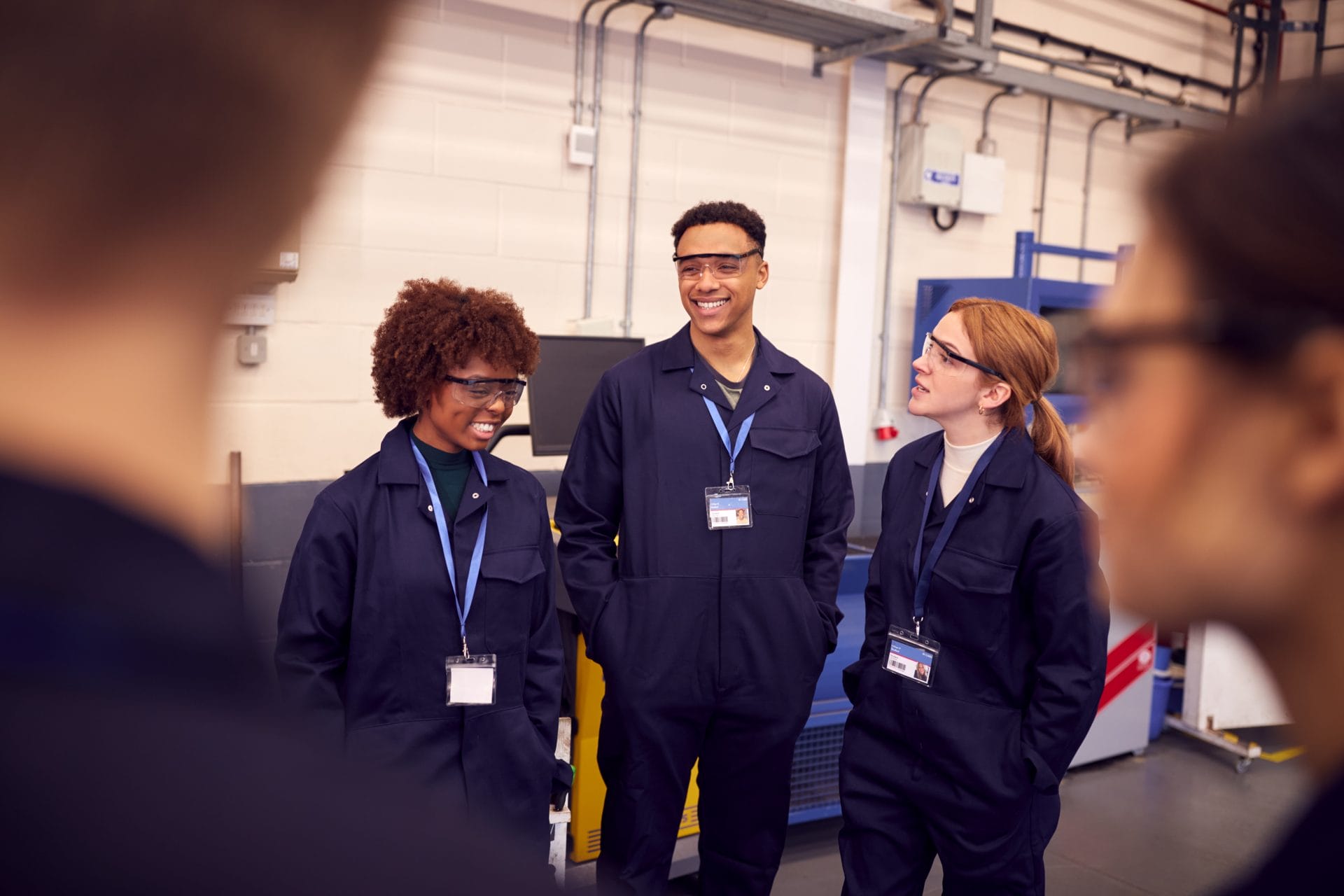Three apprentices in protective work uniforms smiling together in a workshop, representing teamwork and opportunity through paid training.