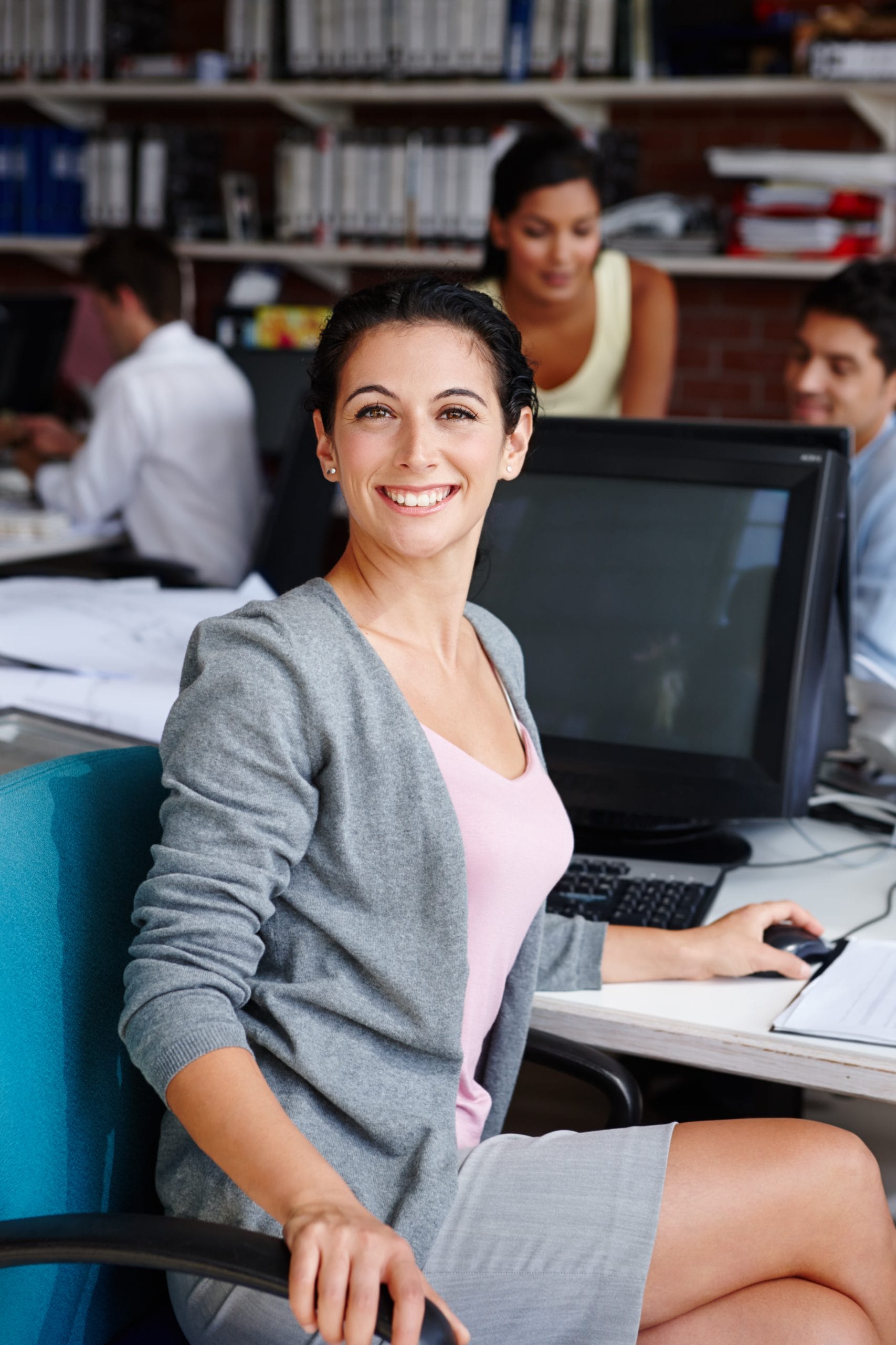 Smiling woman sitting at a computer in a collaborative workspace, representing personalized career support and flexible growth.
