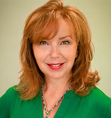 Professional headshot of a woman with auburn hair wearing a green blouse and silver necklace, smiling against a light green background.
