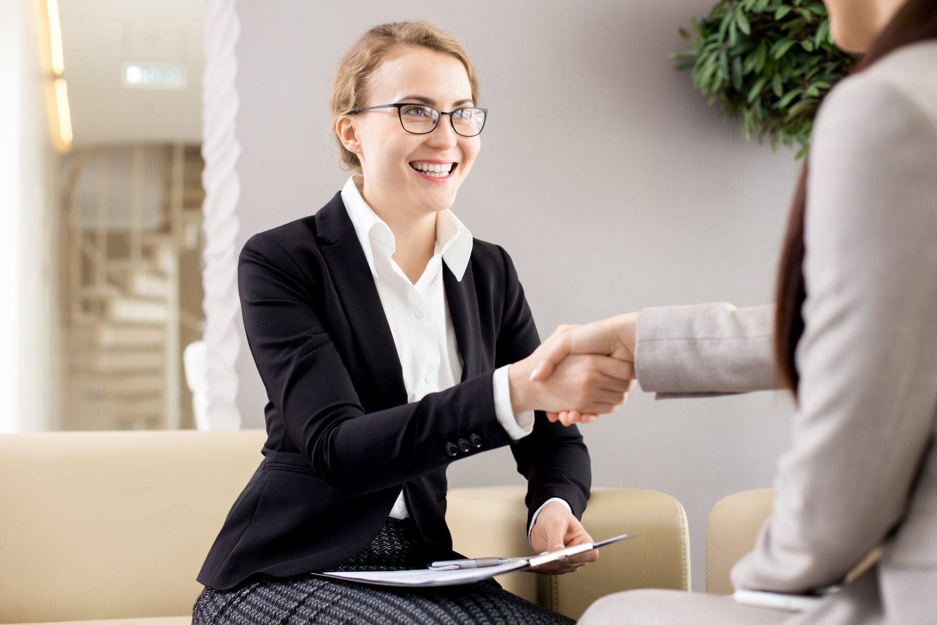 Smiling professional woman in business attire shaking hands across a desk, symbolizing opportunity and collaboration.