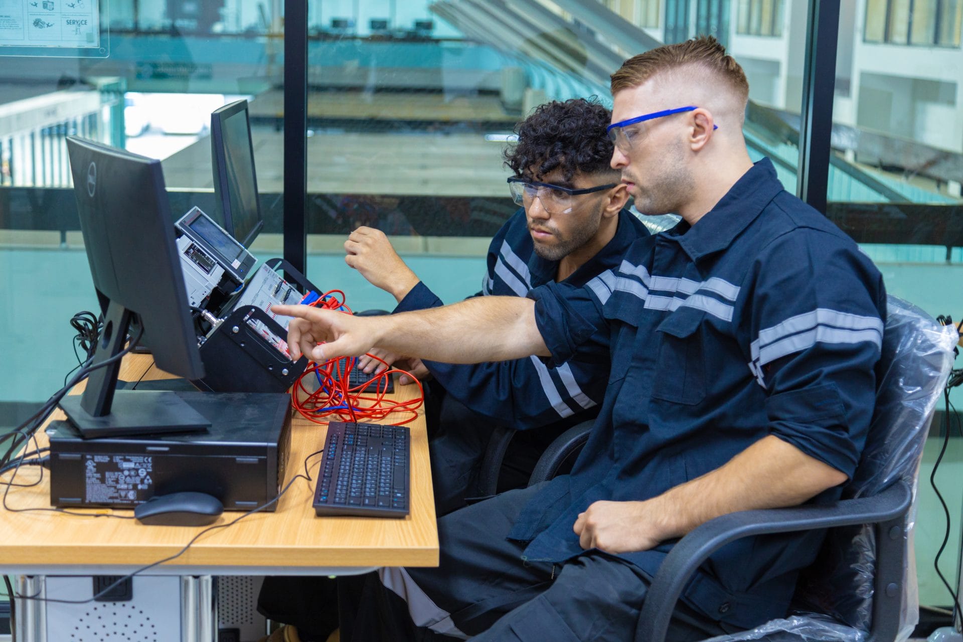 Two workers wearing safety gear collaborating in an industrial setting, representing hands-on training and skill development.