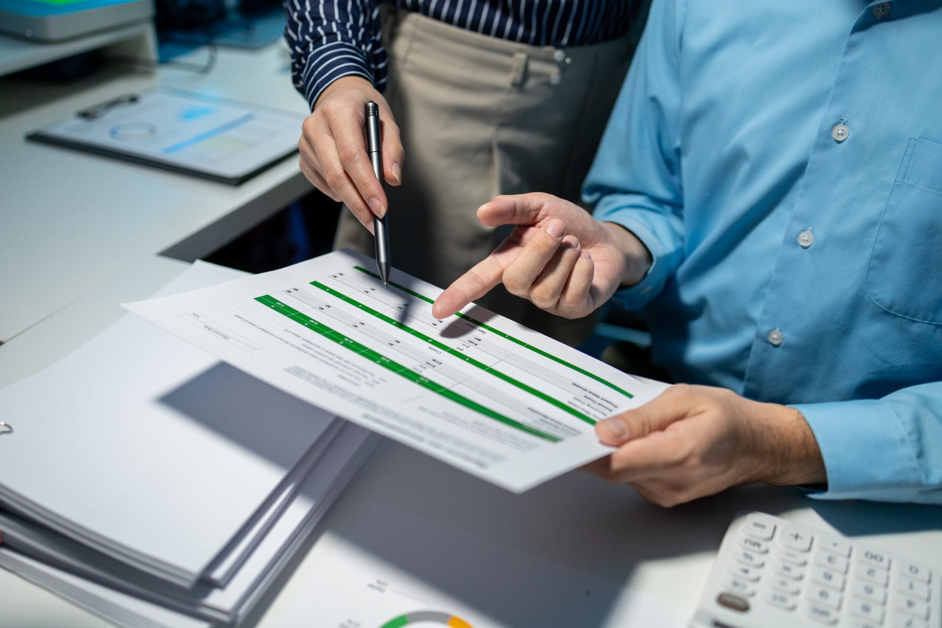 Two professionals reviewing a printed report with charts, discussing performance benchmarks and program alignment.