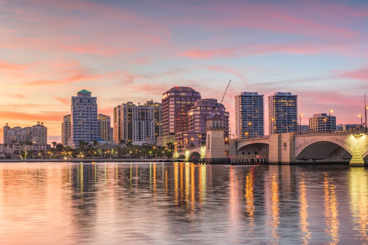 Downtown West Palm Beach skyline at sunset reflecting on the water, symbolizing progress and community growth.