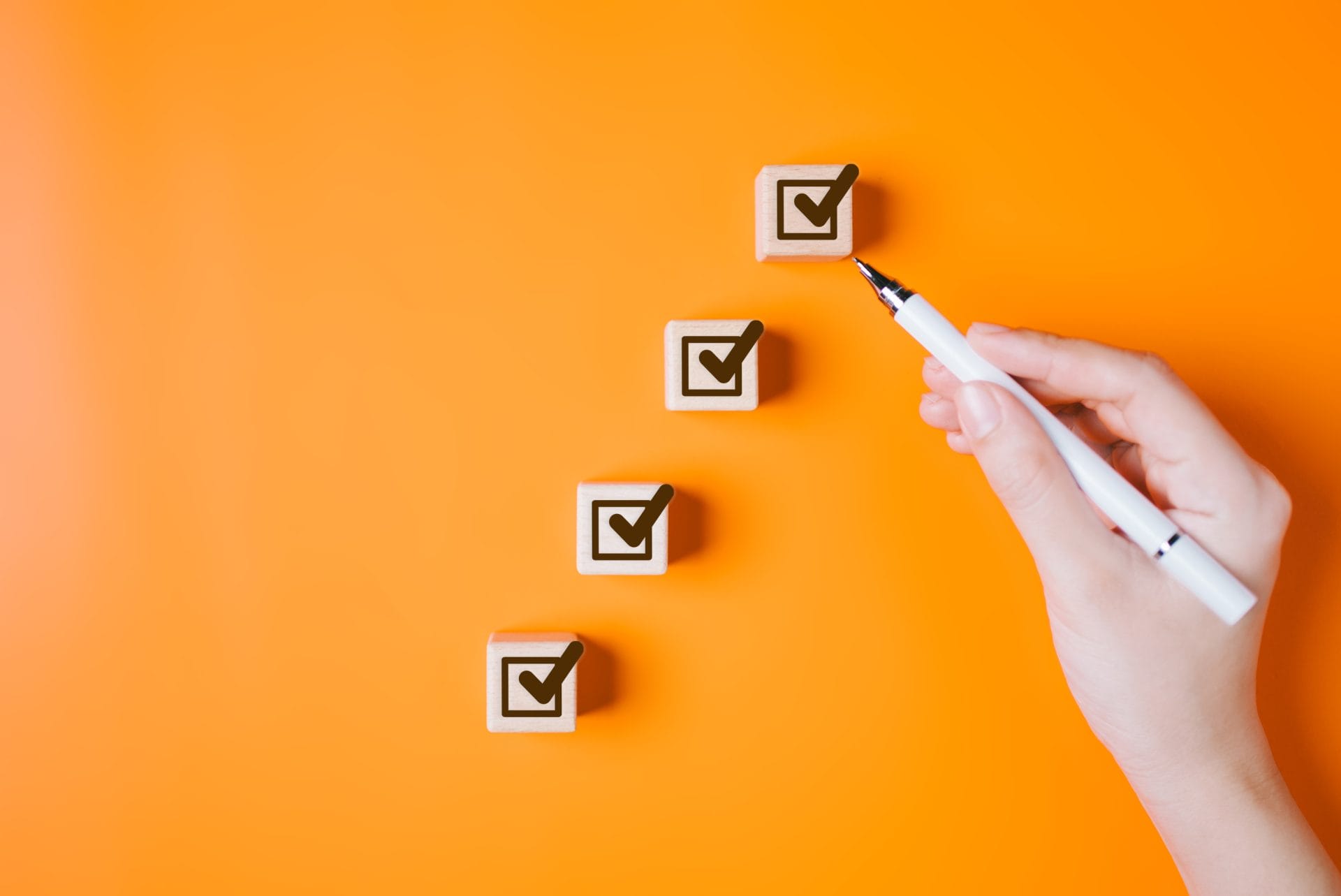 Hand placing wooden blocks with checkmarks on an orange background, symbolizing steps and readiness for success.