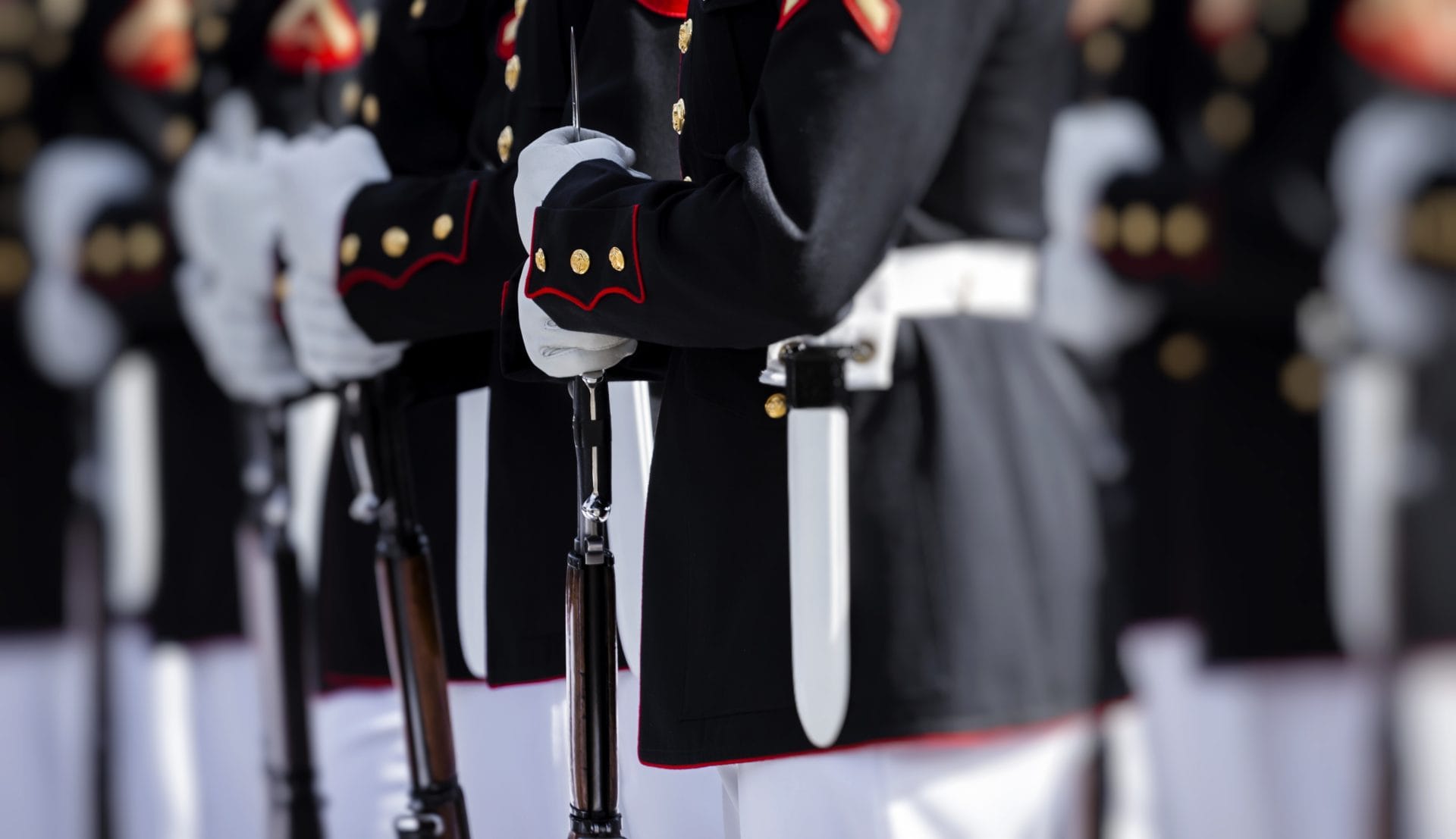 Close-up of uniformed service members standing in formation holding ceremonial swords, representing honor and commitment.