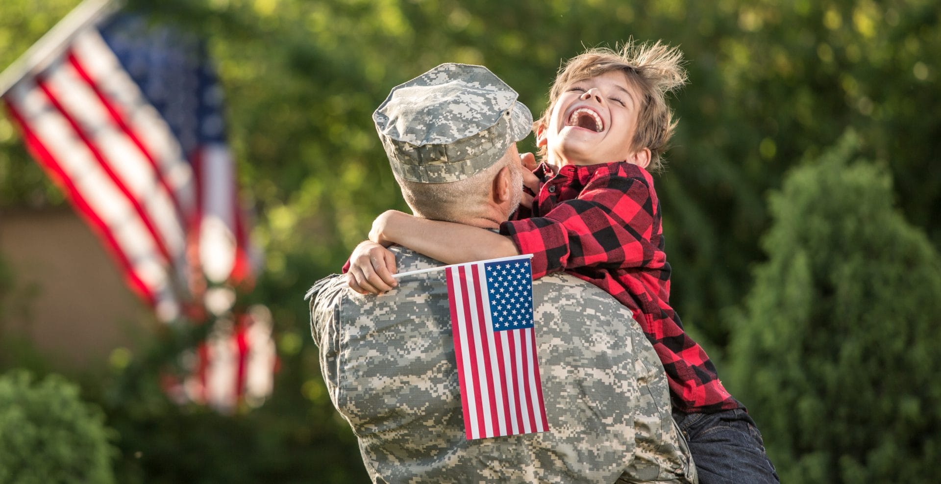 A service member in uniform hugs a smiling child holding an American flag, symbolizing support and new opportunities for veterans and military families.