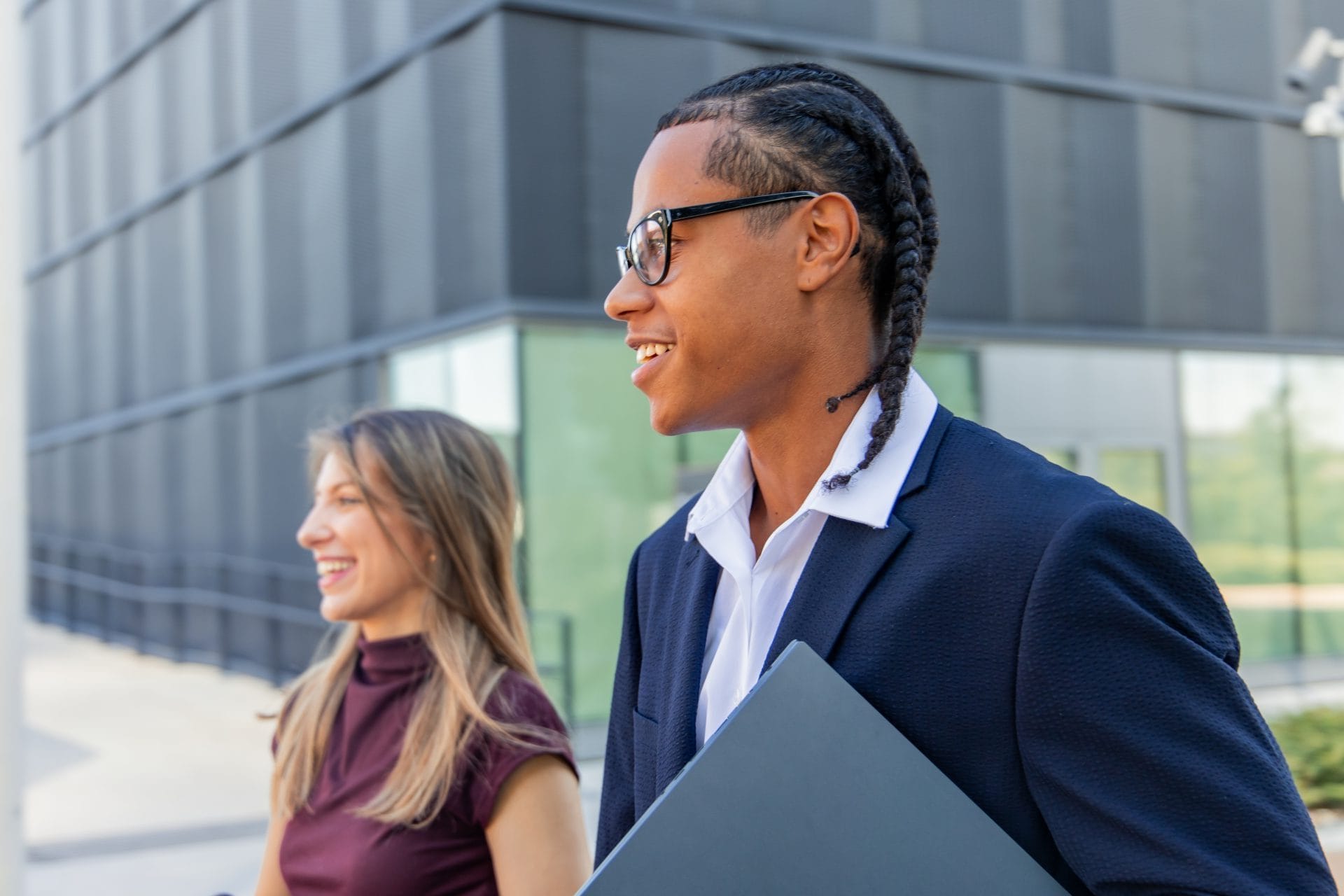 Two young professionals smiling while walking outside a modern building, representing career exploration and opportunity for young adults.