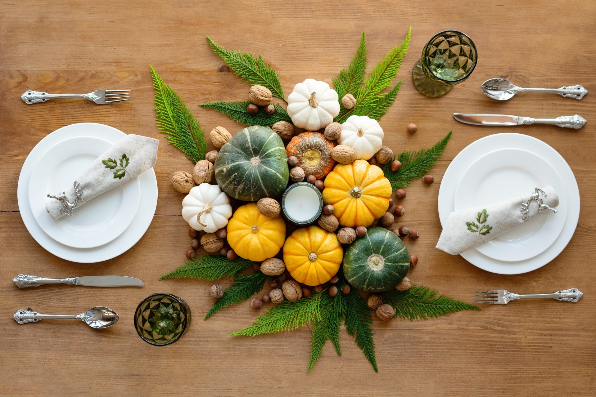 Decorative holiday table arrangement with small pumpkins, pinecones, and greenery, symbolizing seasonal observance and celebration.