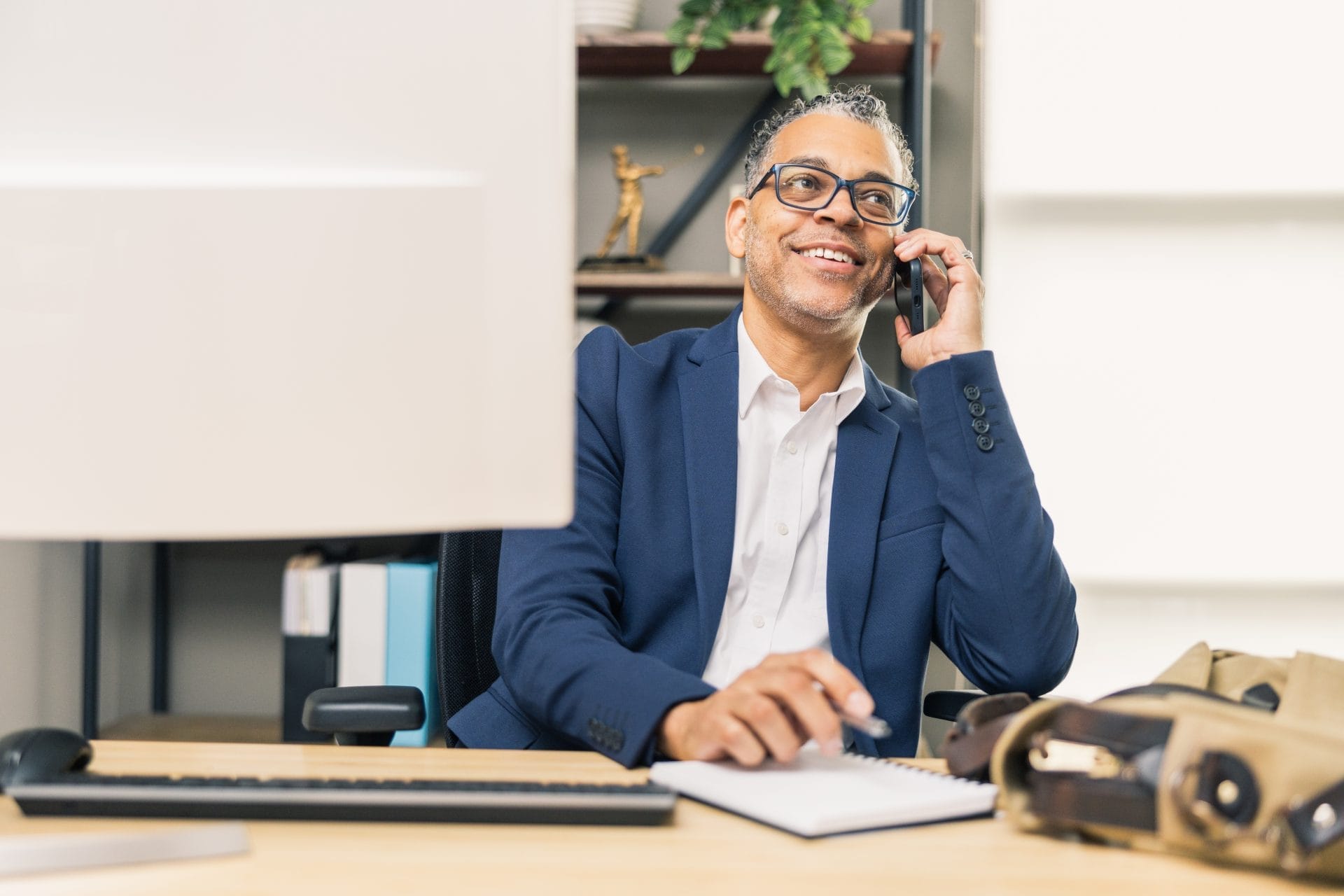 A professional sitting at a desk smiles while talking on the phone, representing a welcoming and purposeful work environment.