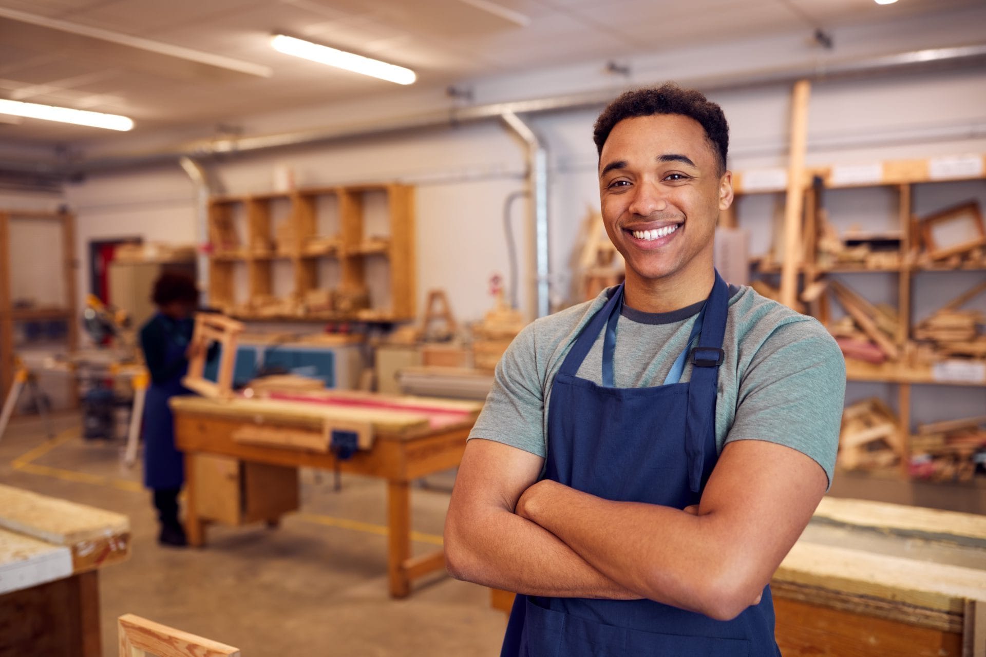 Smiling young apprentice wearing an apron in a workshop, representing hands-on training and skill development.