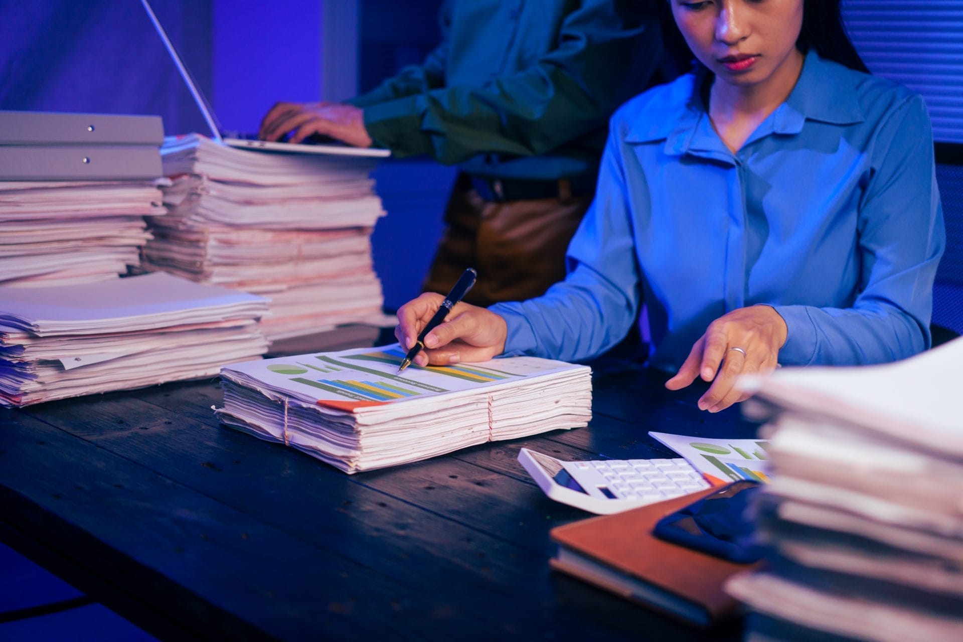 A person reviewing documents at a desk surrounded by organized stacks of files, representing transparency and access to public records.