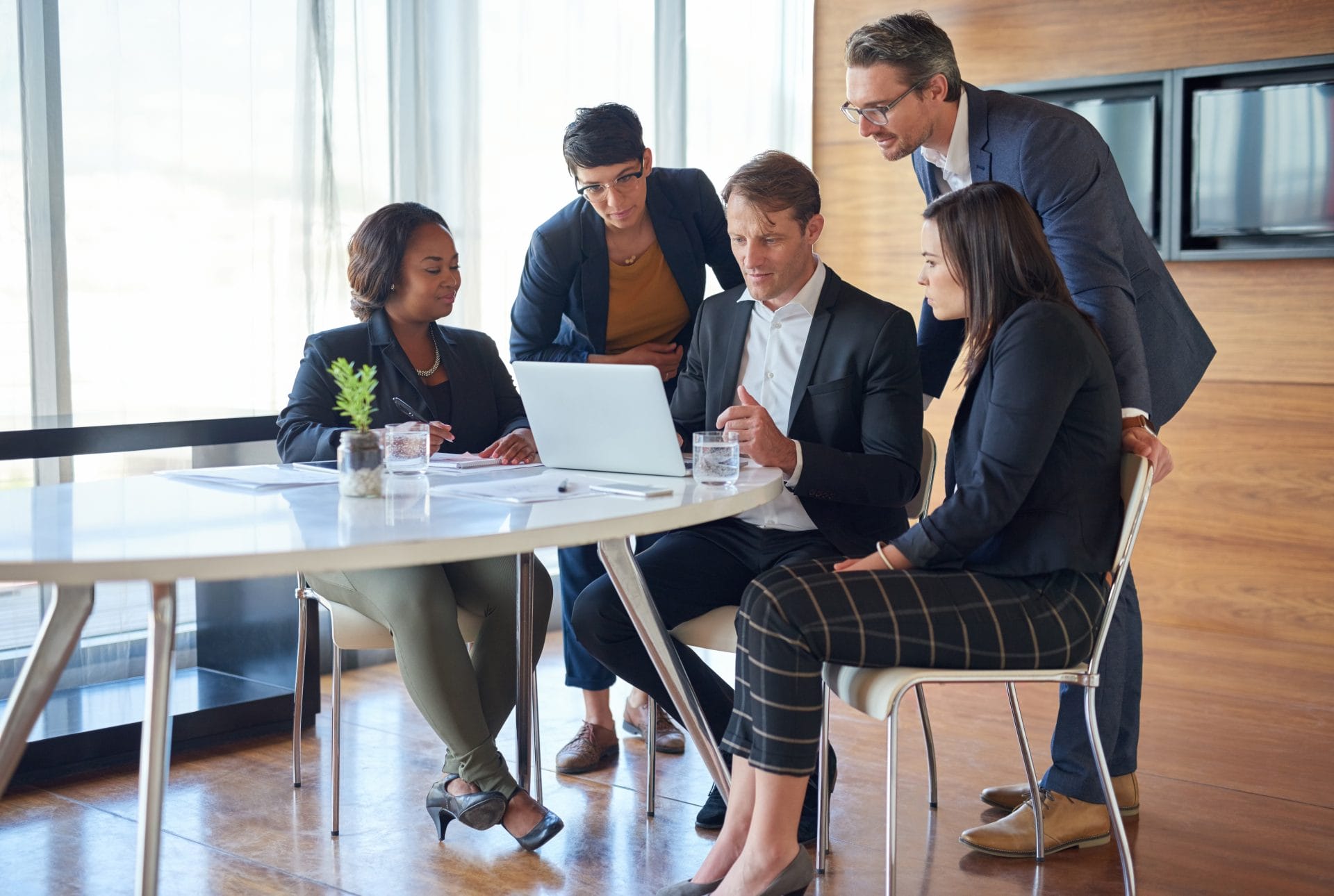 Team of professionals gathered around a laptop in a meeting, discussing workforce and education strategies.