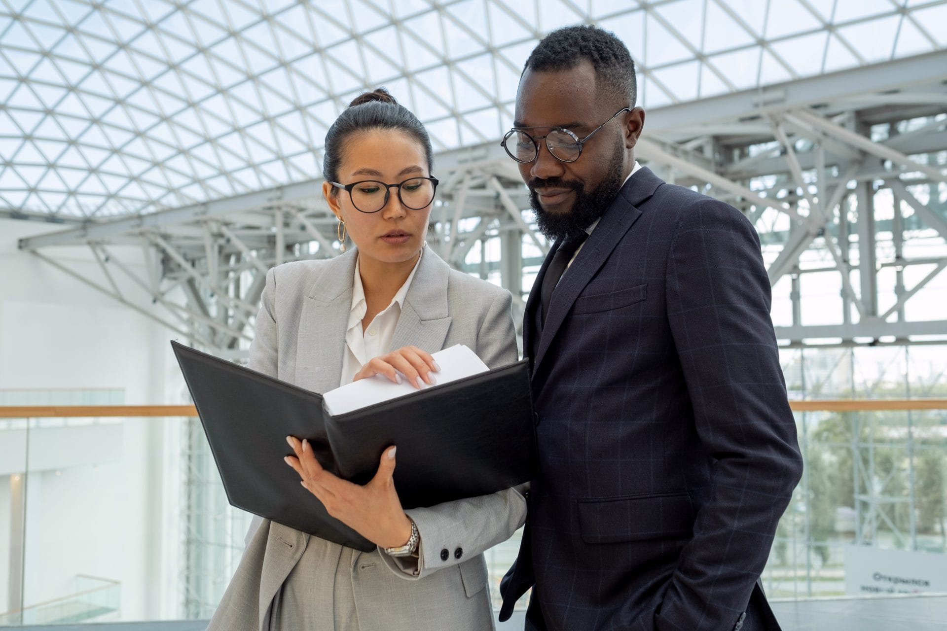 Two business professionals reviewing documents together in a modern building, representing partnership and workforce planning.