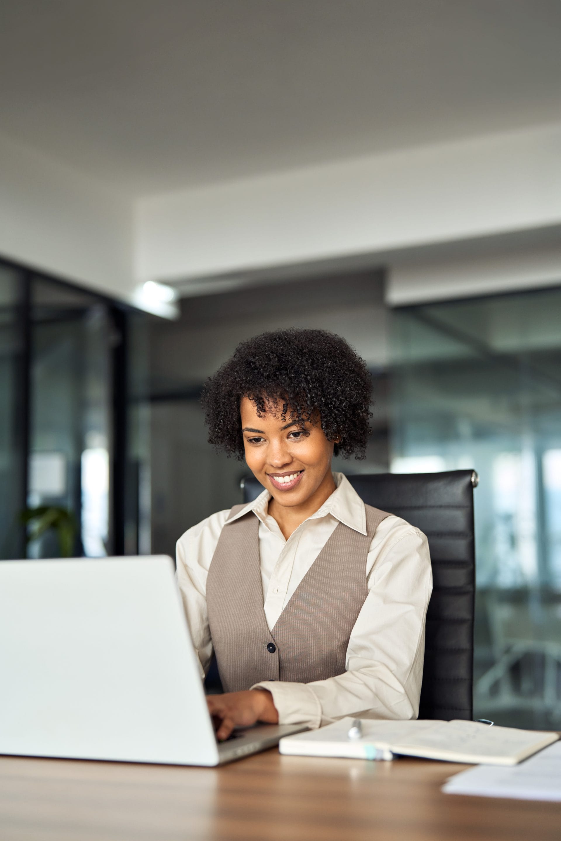 Professional woman smiling while working on a laptop in a modern office, representing connection and support.