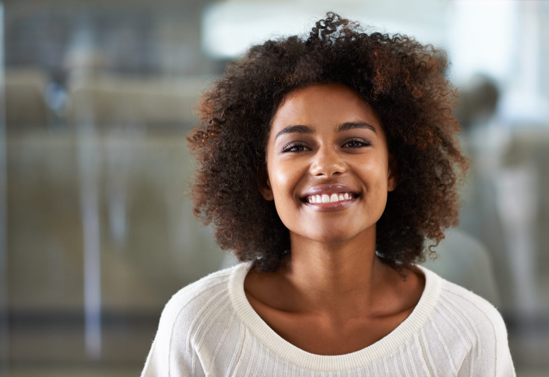 Smiling woman wearing a white sweater in a bright, modern office setting.